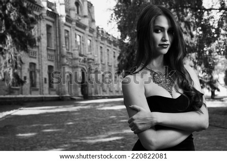 sexy woman in black dress and necklace near old building  black and white photo