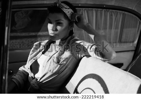pin-up lady with tattoos in old car wearing jeans shirt