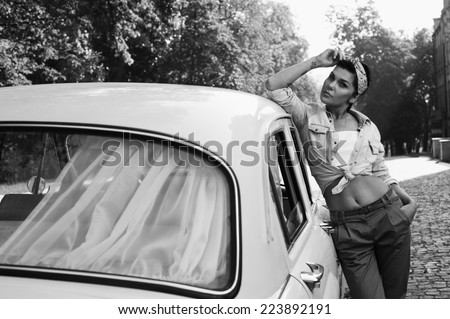 pin-up lady with tattoos near old car wearing jeans shirt