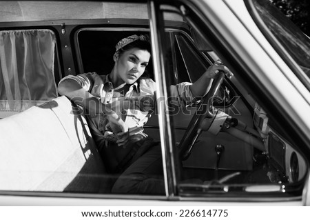 pin-up lady with tattoos in old car wearing jeans shirt