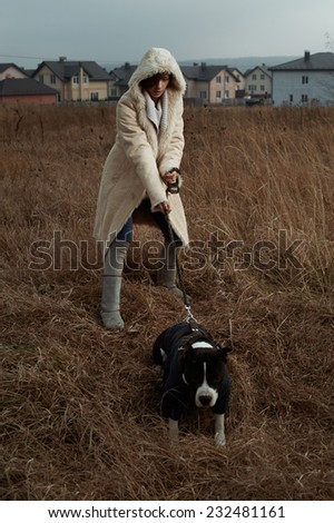 woman walks with staffordshire terrier in fields behind country town
