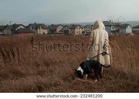 woman standing with staffordshire terrier in fields behind country town