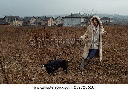 woman walks with staffordshire terrier in fields behind country town