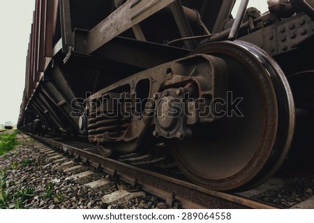 Old rusty freight car on rails in depot. There is some green grass near rails. Freight car is empty.  It is summer but there are some clouds in the sky