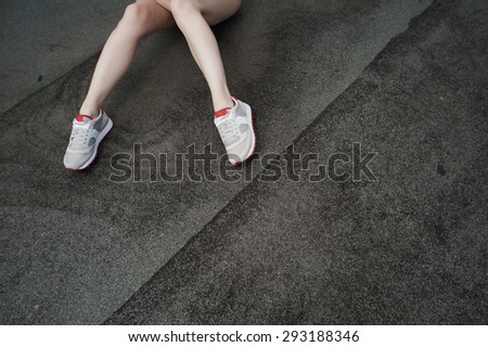 two slim legs in gray sneakers laying half-bent on roofing material or asphalt.