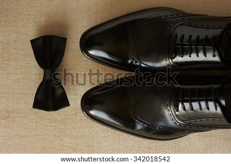 close-up of lightened with natural light men's shoes and bow tie. Shoes and bow tie lying on the wooden floor. They are black