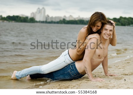 Young couple fooling around on the river bank. man and woman in good shape. They are young and beautiful. they hug. they wear jeans. It is summertime, though the sky is overcast