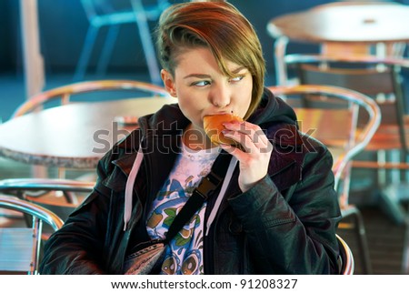 Portrait of stylish blond girl with eats burger on the terrace of the fast food