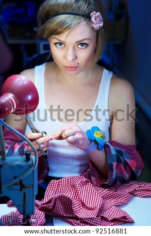 beautiful young seamstress sews a red shirt. girl dressed in a T-shirt. her hair tied with a bandage. It is in her workshop