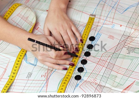 female hands measuring distance with measuring tape and pencil on sewing pattern