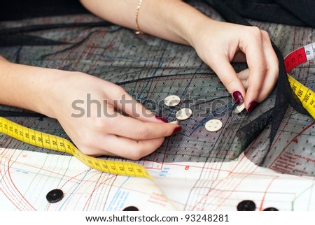 female hands choosing buttons  on cloth over sewing pattern