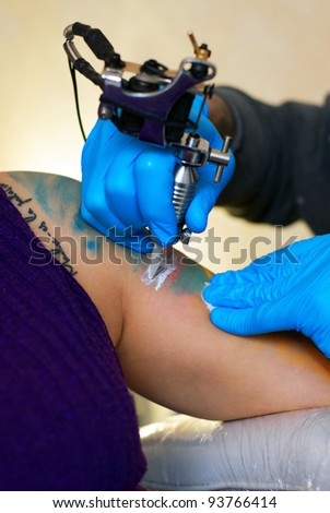 hands of  tattooist create a tattoo on a woman\'s shoulder, close up