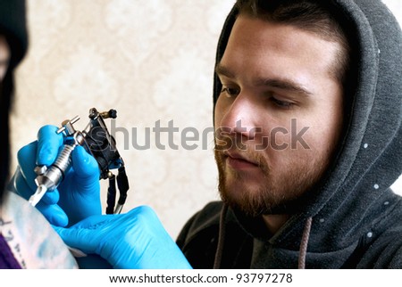 Bearded Caucasian tattooist creates a tattoo on a woman's shoulder, close up