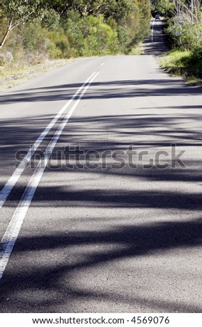 Asphalt Country Road Winding Down A Hill, Sunny Day, Shadows On Street