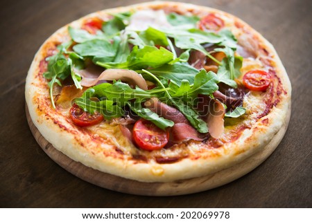 Pizza with prosciutto and arugula (salad rocket) on wooden background