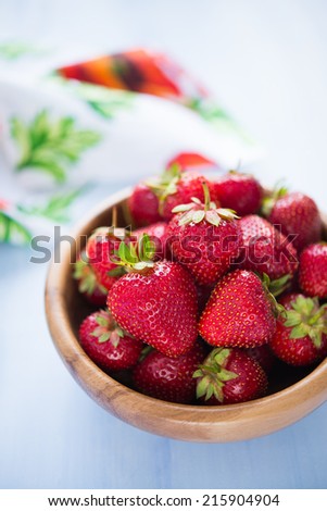 Wooden bowl filled with fresh ripe strawberries on an blue wooden textured table top