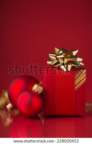 Red gift box with golden ribbons and xmas baubles on red background. Merry christmas.