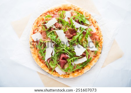 Pizza with prosciutto (parma ham), arugula (salad rocket) and parmesan top view. Italian cuisine.