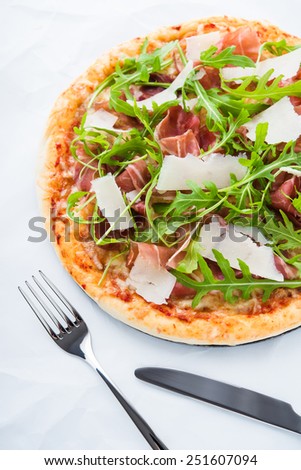 Pizza with prosciutto (parma ham), arugula (salad rocket) and parmesan on white background top view. Italian cuisine.