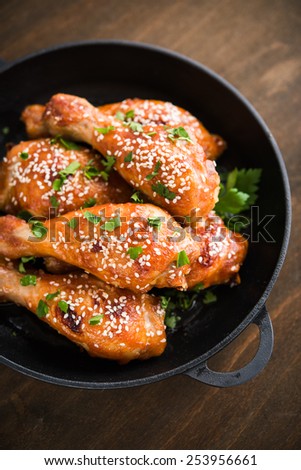 Baked spicy chicken legs with sesame and parsley in cast iron frying pan on dark wooden background.