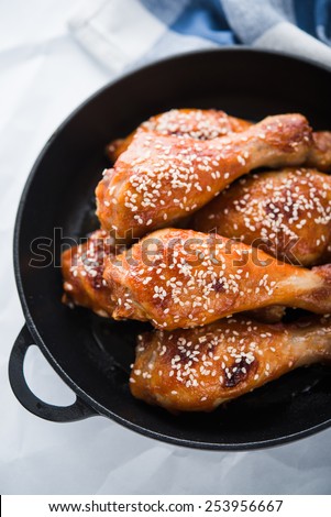 Baked spicy chicken legs with sesame in cast iron frying pan on white background top view.