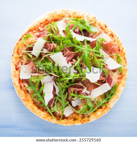 Pizza with prosciutto (parma ham), arugula (salad rocket) and parmesan on blue wooden background top view. Italian cuisine.