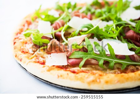 Pizza with prosciutto (parma ham), arugula (salad rocket) and parmesan close up. Italian cuisine.