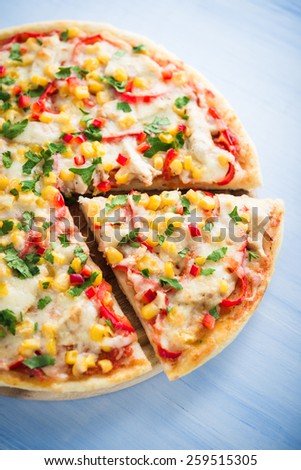Colorful sliced pizza with mozzarella cheese, chicken, sweet corn, sweet pepper and parsley close up. Italian cuisine.