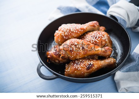 Baked spicy chicken legs with sesame in cast iron frying pan on blue wooden background  close up.