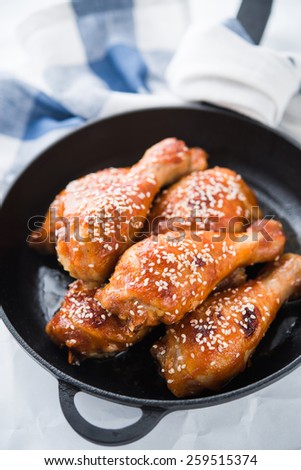 Baked spicy chicken legs with sesame in cast iron frying pan on white background close up.
