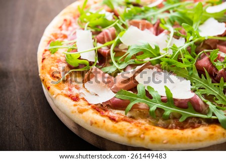 Pizza with prosciutto (parma ham), arugula (salad rocket) and parmesan on dark wooden background close up. Italian cuisine.