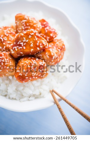 Spicy sweet and sour chicken with sesame and rice on blue wooden background. Oriental food.