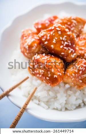 Spicy sweet and sour chicken with sesame and rice on blue wooden background close up. Oriental food.