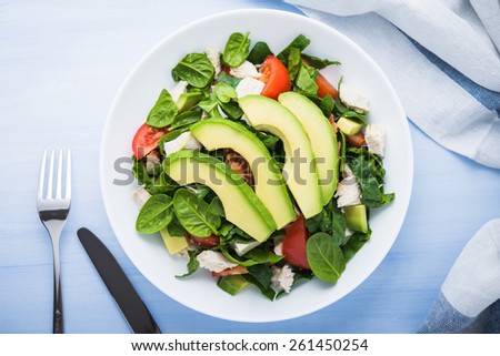 Fresh salad with chicken, tomatoes, spinach and avocado on blue wooden background top view. Healthy food.