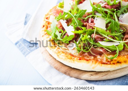 Pizza with prosciutto (parma ham), arugula (salad rocket) and parmesan on blue wooden background close up. Italian cuisine.