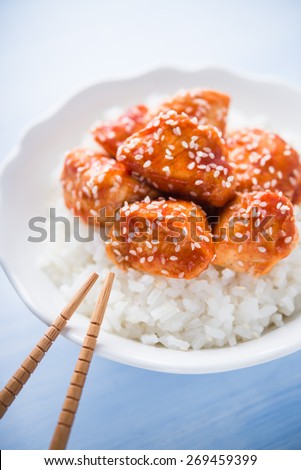 Spicy sweet and sour chicken with sesame and rice on blue wooden background. Oriental food.