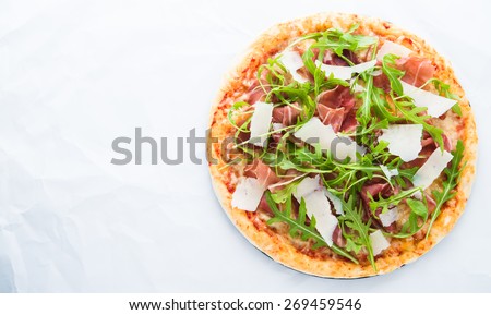 Pizza with prosciutto (parma ham), arugula (salad rocket) and parmesan on white background top view. Italian cuisine. Space for text.