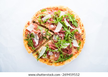 Sliced pizza with prosciutto (parma ham), arugula (salad rocket) and parmesan on white background top view. Italian cuisine.