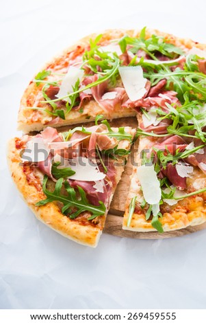 Sliced pizza with prosciutto (parma ham), arugula (salad rocket) and parmesan on white background close up. Italian cuisine.