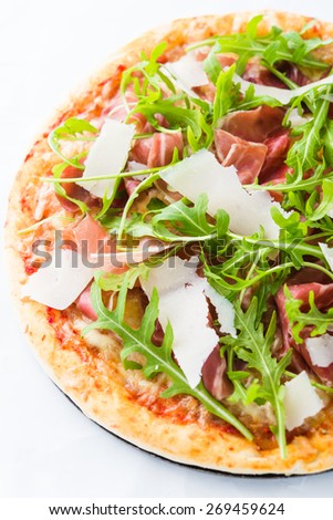Pizza with prosciutto (parma ham), arugula (salad rocket) and parmesan on white background. Italian cuisine.
