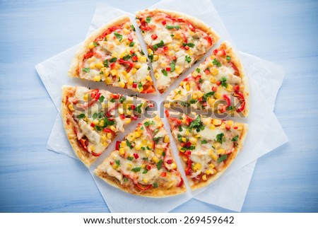 Colorful sliced pizza with mozzarella cheese, chicken, sweet corn, sweet pepper and parsley close up top view. Italian cuisine.