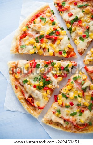 Colorful sliced pizza with mozzarella cheese, chicken, sweet corn, sweet pepper and parsley close up top view. Italian cuisine.