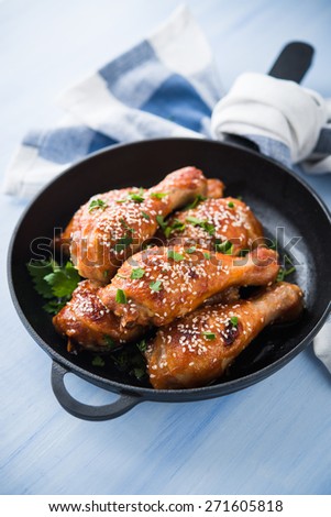 Baked spicy chicken legs with sesame and parsley in cast iron frying pan on blue wooden background close up.