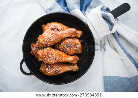 Baked spicy chicken legs with sesame in cast iron frying pan on white background top view.