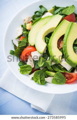 Fresh salad with chicken, tomatoes, spinach and avocado on blue wooden background close up. Healthy food.