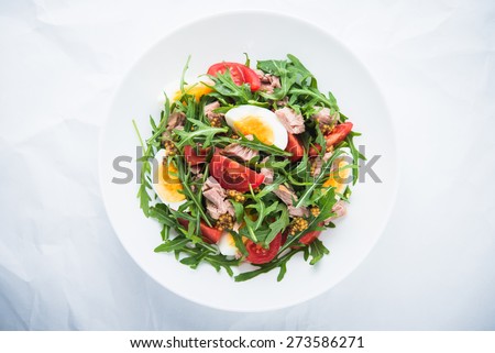 Fresh salad with tuna, tomatoes, eggs, arugula and mustard on white textured background top view. Healthy food.