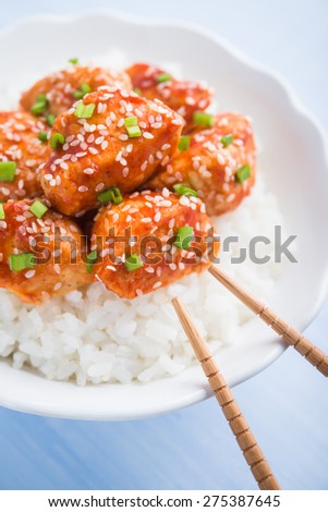 Spicy sweet and sour chicken with sesame and rice close up on blue background. Oriental food.