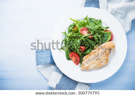 Roasted chicken breast and fresh salad with tomato and greens (spinach, arugula) top view on blue wooden background. Healthy food.