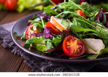 Fresh salad with chicken, tomatoes and mixed greens (arugula, mesclun, mache) on wooden background close up. Healthy food.
