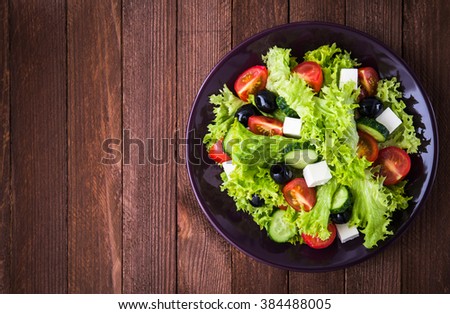 Greek salad (lettuce, tomatoes, feta cheese, cucumbers, black olives) on dark wooden background top view. Space for text. Healthy food.